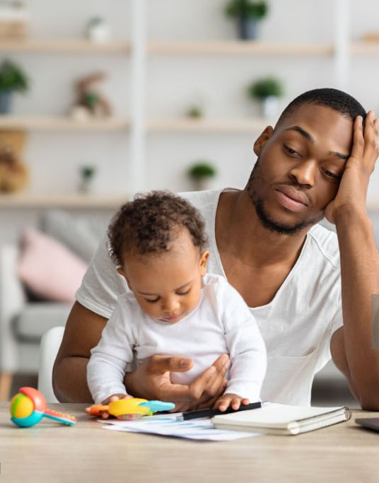 An exhausted father carrying a baby that is still very much active-playing with toys