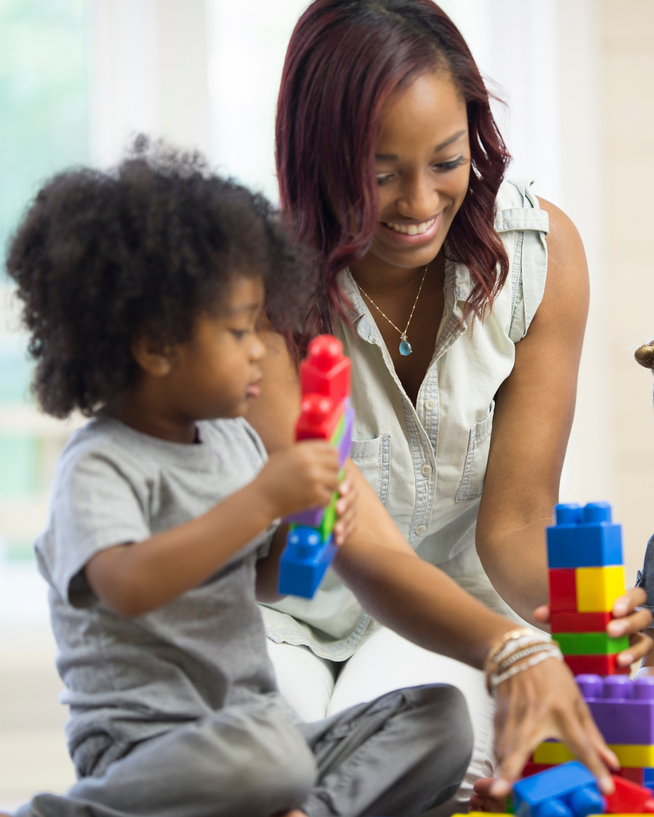 Child and woman smiling, building with colorful toy blocks in a bright room. The mood is playful and joyful.