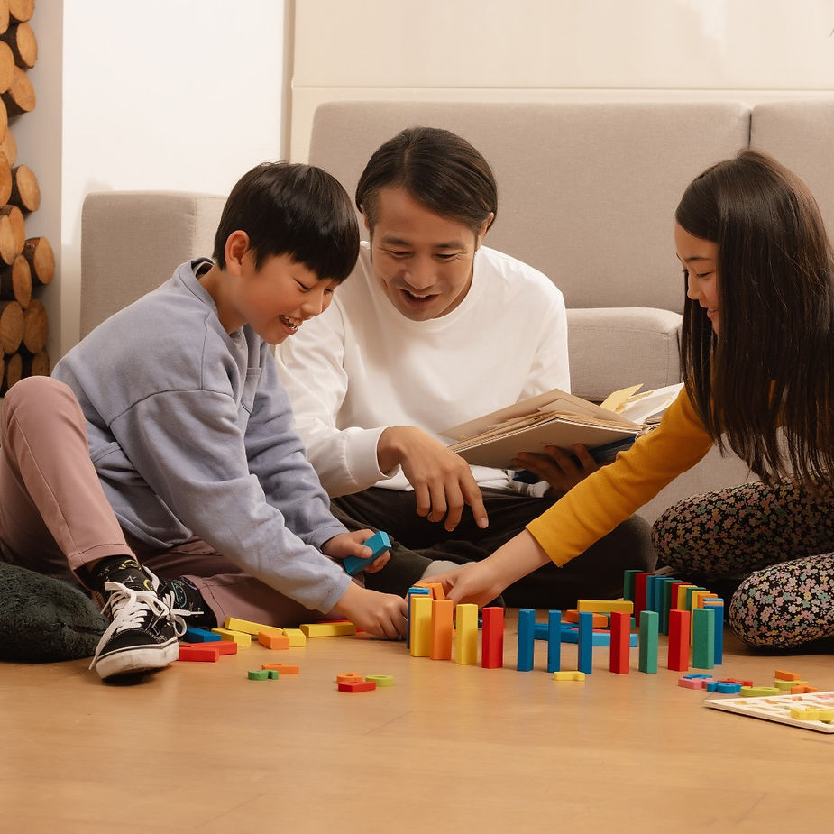 Father and two kids play with colorful blocks on a living room floor.