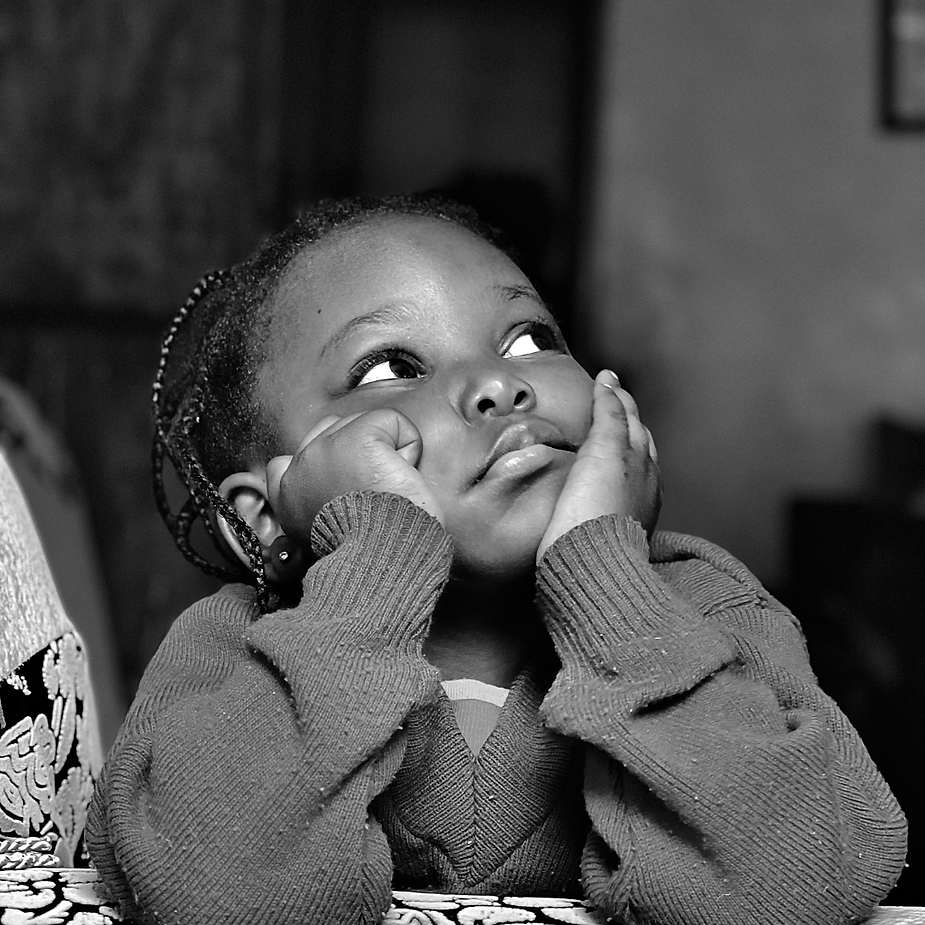 Child with braided hair, resting chin on hands, looking upward in a thoughtful pose.