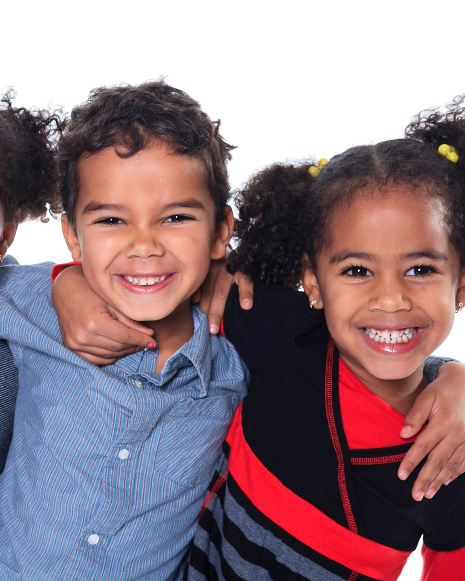 Two smiling children hug, wearing colorful outfits, against a white background. Both display joyful expressions and vibrant energy.