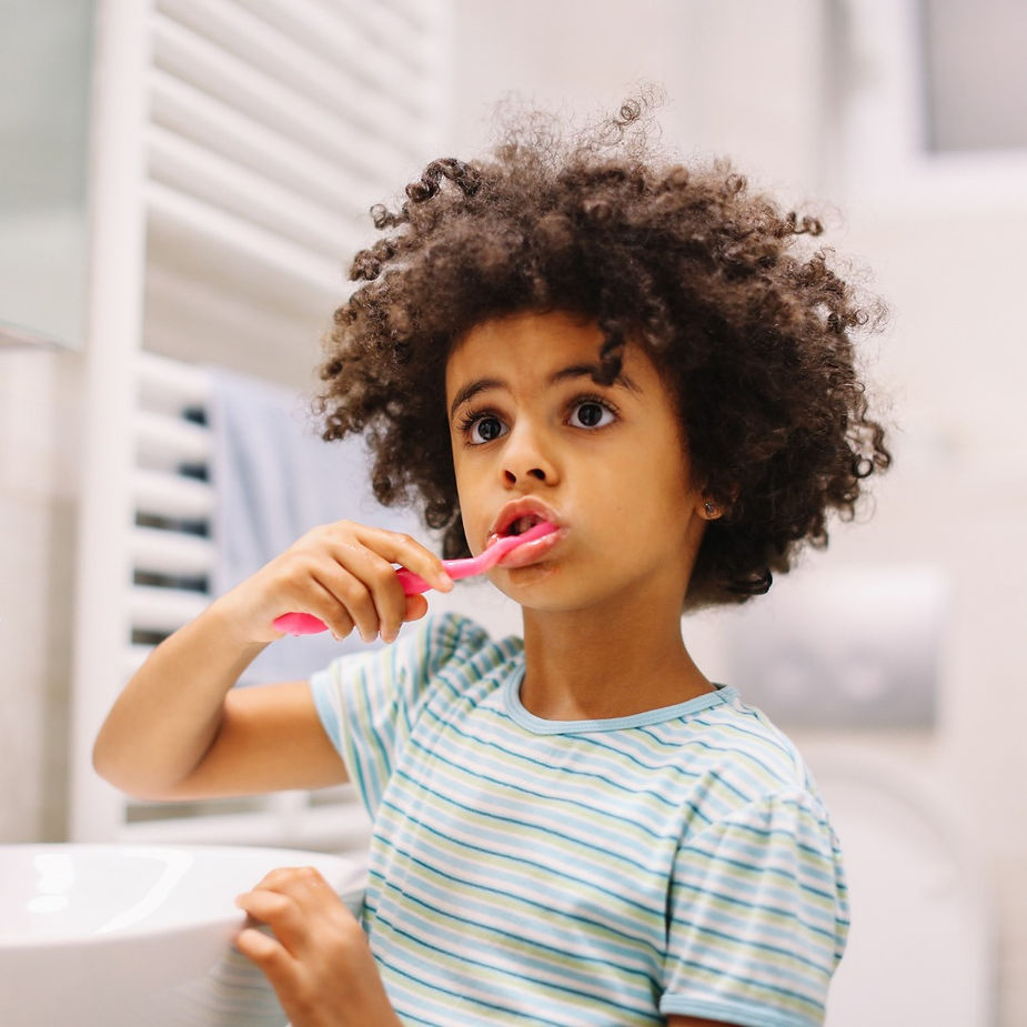 Child brushes teeth with pink toothbrush with a curious expression on his face