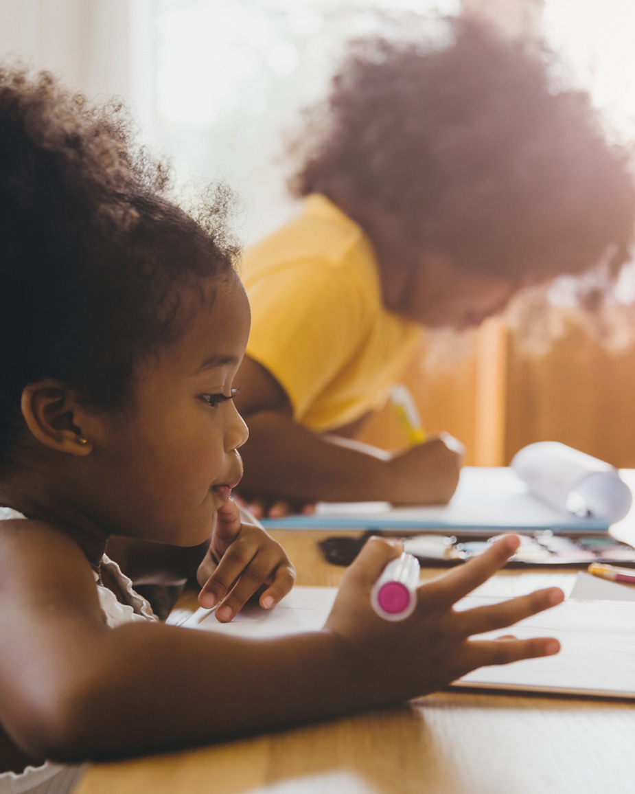 Two children drawing indoors while holding markers.