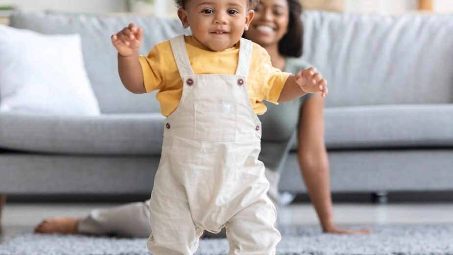 A toddler takes first steps on wooden floor.